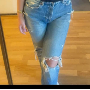 Blå slitna straight jeans - Säljer ett par ljusblå jeans med raka ben och slitna detaljer vid knäna. Jeansen har klassisk femficksdesign och normal passform. Perfekta för en avslappnad och trendig look.