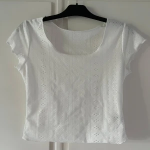Vit broderad blus - Superfin vit blus med broderade detaljer och små hålmönster. Toppen har rundad halsringning och korta ärmar. Aldrig använd då den är lite stor i storleken, skulle tippa på S/M