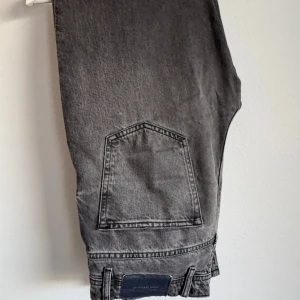River Island svårtgråa jeans straight fit - Säljer ett par Wood jeans i snyggt svartgrått denim. Klassisk femficksmodell med raka ben och normal passform. Jeansen har en mörk tvätt och är perfekta för en avslappnad stil.