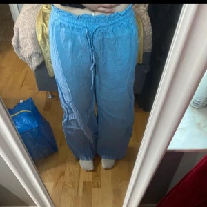 Blå vida linnebyxor med snörning - Säljer ett par ljusblå linnebyxor med resår i midjan samt snörning från DANI.  Säljer då de är för stora för mig och därför aldrig kommit till användning. 