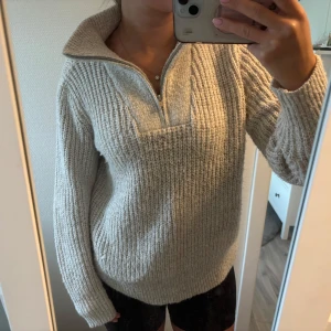 Beige/grå stickad half zip tröja - Supermysig beige stickad tröja med half zip och hög krage, perfekt för kyliga dagar. Snygg att bära både öppen och stängd i halsen. 