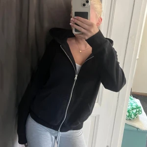 Svart hoodie med dragkedja - Svart hoodie med huva och hel dragkedja framtill. Tröjan har långa ärmar, två fickor och en avslappnad passform. Perfekt för chill dagar eller när du vill ha en enkel och stilren look. Gjord i mjukt bomullsmaterial💗