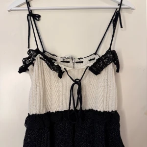 Stickad svartvit topp - Supersöt stickad topp i svart och vitt med smala axelband, snörning framtill och virkade svarta spetsdetaljer. 
