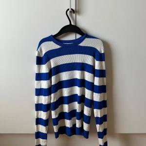 Randig blå och vit ribbad tröja - Säljer en ribbad långärmad tröja med breda blå och vita ränder. Tröjan har rund halsringning och är i ett stretchigt material som sitter snyggt på kroppen. Perfekt för dig som gillar en klassisk men ändå chill stil.