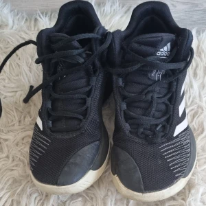 Svarta Adidas sneakers strl 36 - Svarta Adidas sneakers med klassiska vita ränder på sidorna. Skorna har snörning, rund tå och platt sula. Ovandelen är i textil och syntet, vilket ger en sportig och modern look. Perfekta för dig som gillar stilrena och bekväma skor.