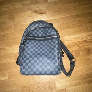 Louis Vuitton rutig ryggsäck i skinn - Säljer en snygg ryggsäck från Louis Vuitton i svart och grått med klassiskt rutigt mönster. Väskan har justerbara axelremmar, dragkedja och flera fack. Materialet är skinn och textil, perfekt för dig som vill ha en stilren och lyxig look. Använt den ganska mycket men det är inga problem med den men därefter kommer priset