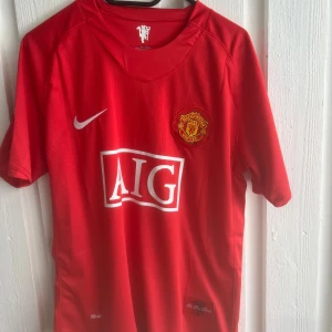Manchester United Ronaldo 7 Nike tröja - Klassisk röd Manchester United matchtröja från Nike med AIG som sponsor på bröstet och klubbmärke broderat. På ryggen står det Ronaldo och nummer 7 i vitt. Tröjan är kortärmad och tillverkad i lätt, ventilerande material perfekt för fotboll eller supporterliv.