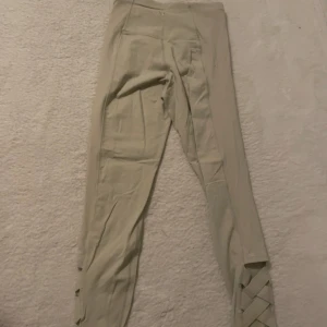 Beige leggings med snörning från stadium  - Snygga beige leggings från stadium med hög midja och cool snörningsdetalj längst ner på benen. Stretchigt material som sitter skönt och följer kroppen. Perfekta för träning eller chill. Diskret logga bak på linningen.