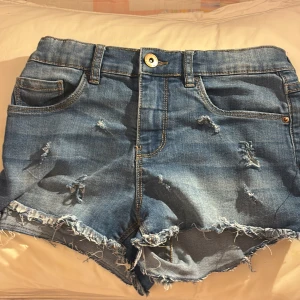Blå jeansshorts med slitningar - Snygga blå jeansshorts från LAB Industries med slitna detaljer och fransig kant. Klassisk femficksmodell med normal passform och låg midja. Perfekta för sommardagar när du vill ha en chill och trendig look. Kontakta om ni har någon fråga.