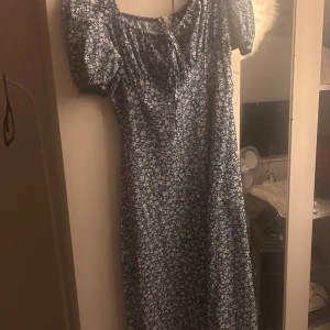 Blommig blå klänning med puffärm - Supersöt blå klänning med vitt blommönster från shein. Klänningen har korta puffärmar, smockad överdel med knytning och en liten slits framtill. Perfekt för sommarens alla tillfällen och ger en romantisk vibe.