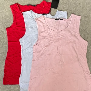 linnen i rosa, rött och ljusblått - Tre enkla och mjuka linnen i olika färger: ett ljusrosa, ett rött och ett ljusblått. Alla är ärmlösa med rund halsringning och tillverkade i ett stretchigt material som känns skönt mot huden. Perfekta att matcha till jeans eller shorts. 15 per stycke. 