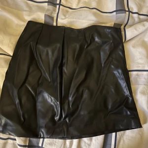 Svart skinnimitation kjol H&M Divided XS - Snygg svart kort kjol i skinnimitation från H&M Divided. Kjolen har en clean och stilren look med lätt glansig yta och figurnära passform. Perfekt för dig som vill ha en edgy vibe till outfiten.