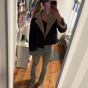 Svart teddyjacka med beige foder - Säljer en svart teddyjacka med beige fuskpälsfoder och bred krage. Jackan har dragkedja, bälte i midjan och uppvikta ärmslut med synligt foder. Snygg croppad modell som passar perfekt till jeans och boots. NY PRIS: 900 
