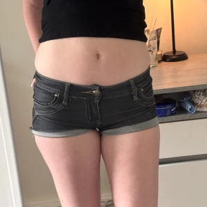 Svarta lågmidjade jeansshorts i denim - Supersnygga svarta jeansshorts från i do do JEANS med låg midja och tight passform. Klassisk femficksmodell med uppvikta benslut och kontrastsömmar. Perfekta för varma sommardagar när du vill ha en edgy look.