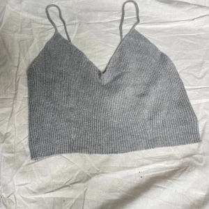 Grå ribbad linnetopp från Bik Bok - Snygg grå ribbad linnetopp från Bik Bok med smala axelband och v-ringad hals. Toppen är croppad och har en mjuk, stretchig känsla tack vare materialmixen av viskos, nylon och elastan. Perfekt att styla med jeans eller kjol för en chill look.