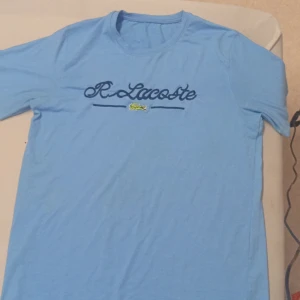 Ljusblå Lacoste t-shirt med brodyr - Snygg ljusblå t-shirt från Lacoste med broderad logga och krokodil på bröstet. Klassisk rund hals och korta ärmar. Perfekt för dig som gillar stilrena och sportiga plagg med en touch av street.