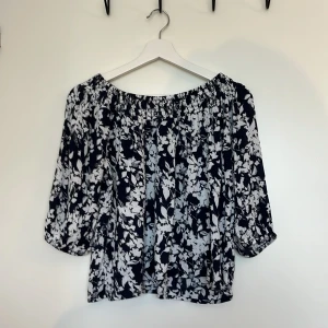 Blommig offshoulder blus Cubus XS - Söt blommig blus i svart och vitt med offshoulder-modell och trekvartsärmar. Blusen har resår vid halsringningen och är tillverkad i ett lätt, luftigt tyg som känns skönt mot huden. Liten defekt vid nedre kant, annars felfri.