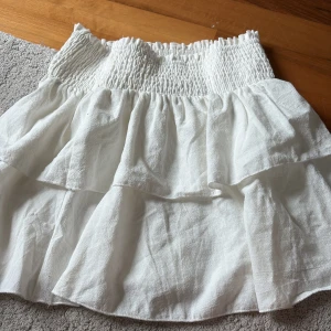 Vit volangkjol  - Supersöt vit kortkjol från SHEIN i storlek XS. Kjolen har smockad midja och flera lager med volanger som ger en flowy och luftig känsla. Perfekt för dig som gillar en feminin och trendig stil.