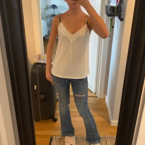 Vit linnetopp med spets från Amisu - Supersöt vit linnetopp från Amisu med tunna axelband och v-ringning dekorerad med spets. Toppen är ärmlös och har en clean, enkel look som passar perfekt till jeans eller kjol. Lätt och luftig, perfekt för varma dagar. Strl S men passar både XS och M💗