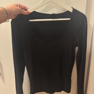 Svart långärmad topp Gina Tricot - En svart långärmad topp från Gina Tricot i storlek M. Modellen har en djup rundad urringning och är figurnära med smala ärmar.  Slits vid handen , se bild!
