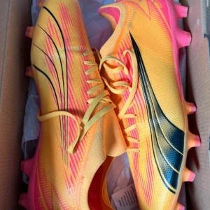 Puma fotbollsskor i gult och rosa - Säljer splitternya fotbollsskor! Snygga och lätta fotbollsskor i en iögonfallande gul/orange färg med rosa och svarta detaljer. Skorna har fasta dobbar som passar perfekt för spel på natur- eller konstgräs. Skorna är helt nya, aldrig använda och levereras i originalkartong.funkar både för konstgräs och naturgräs 