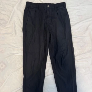 Svarta linnebyxor med resårmidja - Snygga svarta linnebyxor med avslappnad passform och resår i midjan. Byxorna har sidfickor, knäppning fram och bakfickor med knapp. Perfekta för en chill och stilren look.