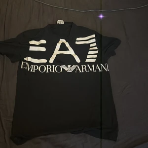 Svart EA7 Emporio Armani t-shirt - Svart t-shirt från EA7 Emporio Armani med stor vit logga och tryck framtill. Klassisk rund hals och korta ärmar. Snygg och stilren design som passar perfekt till jeans eller shorts.