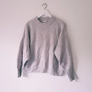 Ljusgrå stickad tröja med pärlor H&M strl M - Supermysig ljusgrå stickad tröja från H&M med pärldetaljer över hela tröjan. Tröjan har rund halsringning, ribbade muddar och lång ärm. Perfekt för lager-på-lager och chill höst- och vinterstil.  Helt skick dock noppror & obehandlad fläck