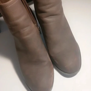 Bruna boots med klack och dragkedja - Snygga bruna boots i skinnimitation med rund tå och kraftig hög klack. Dragkedja på sidan för enkel påtagning. Perfekta för dig som vill ha en stilren och trendig look till höst och vinter.