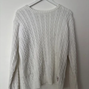Vit stickad tröja Iconic Sport L - Kabelstickad vit tröja från Iconic Sport i storlek Large. Klassisk modell med rund halsringning och ribbade muddar. Perfekt för dig som gillar en clean och tidlös look. Snygg att styla med jeans eller chinos.