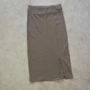 Beige ribbad midikjol från LMTD - Säljer en beige ribbad långkjol från LMTD i storlek XS. Kjolen har en smal passform, diskreta vertikala ränder och en liten slits framtill för extra stilpoäng. Perfekt att matcha med en enkel topp eller hoodie för en chill look. Använt en gång