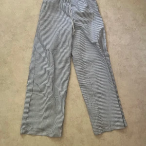 Randiga vida linnebyxor med snörning - Snygga randiga linnebyxor i vitt och blått med vida ben. Byxorna har snörning i midjan och är tillverkade i ett lätt och svalt linnematerial, perfekta för varma dagar. Klassisk look med tunna vertikala ränder.