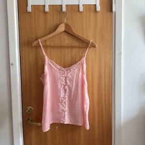 Rosa spetslinne från NA-KD - Supersöt ljusrosa linnetopp från NA-KD med tunna axelband och vacker spetsdetalj längs urringningen och framtill. Toppen har en lös passform och är perfekt för varma dagar. Materialet känns lätt och luftigt💞Säljs pga att jag inte använder den💗
