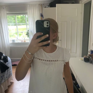 Vit blus med volangärmar och broderi - Superfin vit blus med broderade detaljer och små hålmönster. Blusen har volangärmar och en söt spetsrad över bröstet. Perfekt för en fräsch och somrig look! Luftig och lätt att matcha med jeans eller kjol.