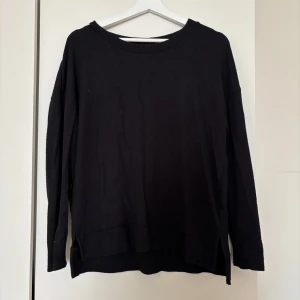 Svart stickad tröja från Hollys - En svart stickad tröja från Hollys i storlek M. Tröjan har rund halsringning, ribbade muddar och slitsar i sidorna för en chill och avslappnad look. Perfekt att slänga på sig när det är kallt ute.