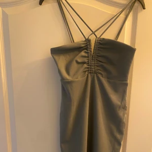 Grön klänning - Snygg grå klänning med smala korsade axelband och rynkdetalj framtill. Axelbandslös design som ger en stilren och modern look. Perfekt för dig som gillar minimalistisk stil och vill sticka ut med enkla detaljer. Har enbart använts en gång.