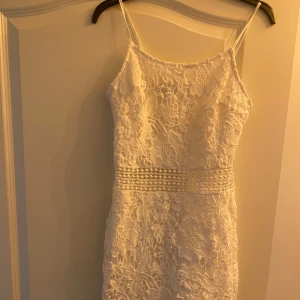 Vit spetsklänning med smala axelband - Superfin vit kortklänning med smala axelband och vackert blommigt spetsmönster. Midjan har dekorativa detaljer och klänningen har en feminin, figurnära passform. Perfekt för somriga tillfällen eller studentfirande! Pris kan diskuteras vid snabb affär.