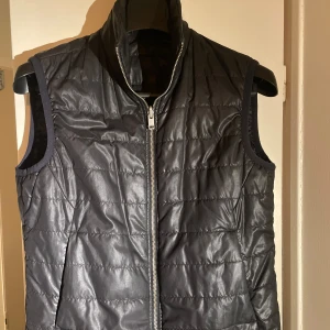 Svart väst från J.Lindeberg - Snygg svart väst från J.Lindeberg med dragkedja framtill. Perfekt för lager-på-lager under kyliga dagar. Västen har en stilren design och är lätt att matcha med olika outfits. Två fickor och två innerfickor, vid ev frågor eller funderingar är det bara att kontakta ☺️