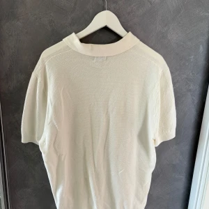 Vit stickad pikétröja från H&M - Säljer en stilren vit pikétröja från H&M med korta ärmar och klassisk krage. Tröjan är stickad i bomull och har knappar framtill. Perfekt för en clean och avslappnad look under vår och sommar.
