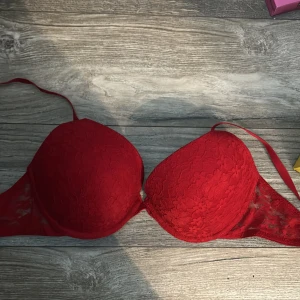 Röd spets BH - Snygg röd BH med blommig spets och vadderade kupor. Axelbandslös design och transparent spets. Perfekt för att styla under en öppen skjorta eller kavaj. C-D kupa