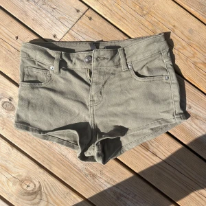 Militärgröna jeansshorts med fickor - Snygga lågmidjade militärgröna jeansshorts med klassisk femficksdesign och bälteshällor. De har låg midja och korta ben, perfekta för varma dagar. Materialet är slitstarkt och mjukt bomullstyg som ger en skön känsla. Passar dig som gillar en enkel och clean stil.