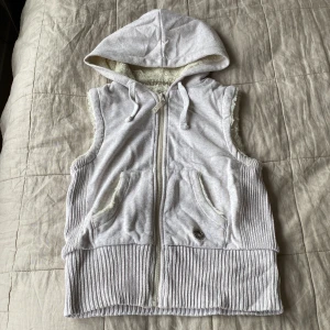 Vit huväst från Denim Co med foder - Mysig grå väst med huva och dragkedja framtill. Västen har ribbade detaljer vid nederkant och fickor, samt mjukt fleecefoder i huvan. Har små noppror över hela men annars i fint skick! Står ingen storlek men skulle säga typ S.