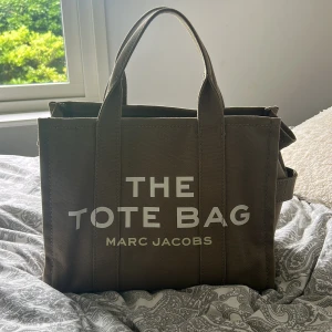 Marc Jacobs Tote Bag i militär grön canvas - Säljer en snygg militär grön Tote Bag från Marc Jacobs i kraftig canvas. Väskan har tydlig logga framtill, dubbla handtag och innerfack med dragkedja. Perfekt storlek för att få plats med allt du behöver och passar till många olika outfits.
