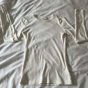 Vit ribbad långärmad tröja Gina tricoot - Säljer en vit långärmad tröja från Weekday i ribbad bomull. Tröjan har en slim passform och rund halsringning, perfekt att styla med jeans eller kjol. Enkel och clean look som funkar året runt.