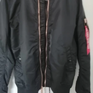 Svart bomberjacka med dragkedja - Snygg svart bomberjacka med dragkedja framtill och ribbade muddar. Jackan har långa ärmar och en klassisk design med fickor på sidorna. Perfekt för en cool och avslappnad stil.