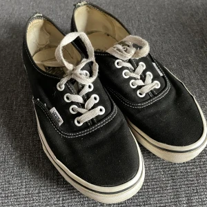 Svarta Vans - Klassiska svarta sneakers från Vans med vit sula och snörning. Perfekta för en avslappnad stil och passar till det mesta. De har en enkel och tidlös design som aldrig går ur mode. Välanvända, men kan säkert glädja nån mer ⭐️
