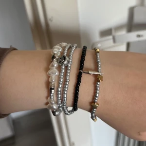 Flera armband med pärlor och detaljer - Säljer ett set av armband med olika stilar. Ett armband har vita pärlor och ett litet smiley-ansikte, ett annat är svart med små pärlor, och ett tredje har silverfärgade pärlor med guldiga detaljer. Perfekt för att mixa och matcha!