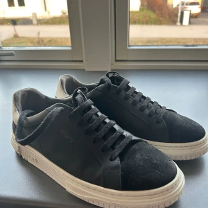 Svarta sneakers från Axel Arigato - Snygga svarta sneakers från Axel Arigato med vit sula och svart snörning. Skorna har en stilren design med en kombination av skinn och mocka. Perfekta för en trendig look. Nästan aldrig använda, ett få tal gånger