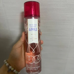 Winter Candy Apple Fine Fragrance Mist - Fräsch och fruktig doftspray från Bath & Body Works. Winter Candy Apple kommer i en genomskinlig flaska med röd kork och dekorativa vita mönster. Perfekt för en uppfriskande känsla med en söt och fruktig doft av äpple.