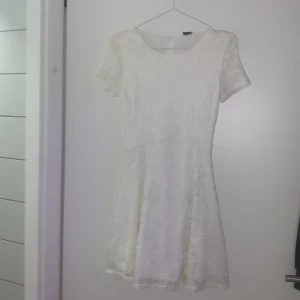 Vit spetsklänning med korta ärmar - Säljer en söt vit spetsklänning med korta ärmar och dragkedja i ryggen. Perfekt för sommarens festligheter. Klänningen har en fin passform och är täckt av vacker spets.